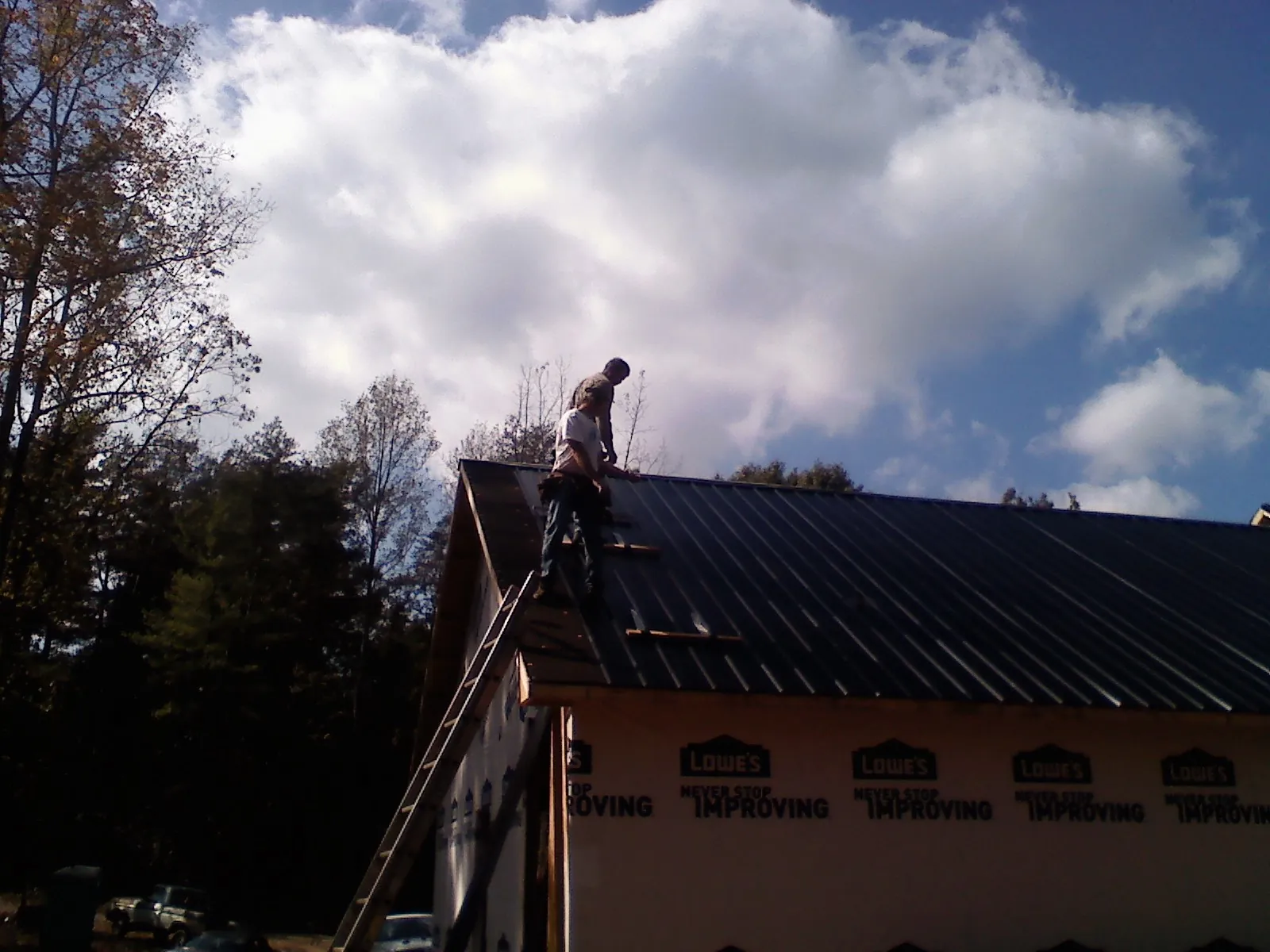 Roofer fastening dark metal panels high against a cloudy sky, from a Roof Inspection job in Ephraim